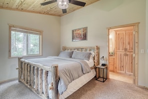 Quarto com estrutura de cama de madeira, janela com persianas, pintura na parede e guarda-roupa de madeira.