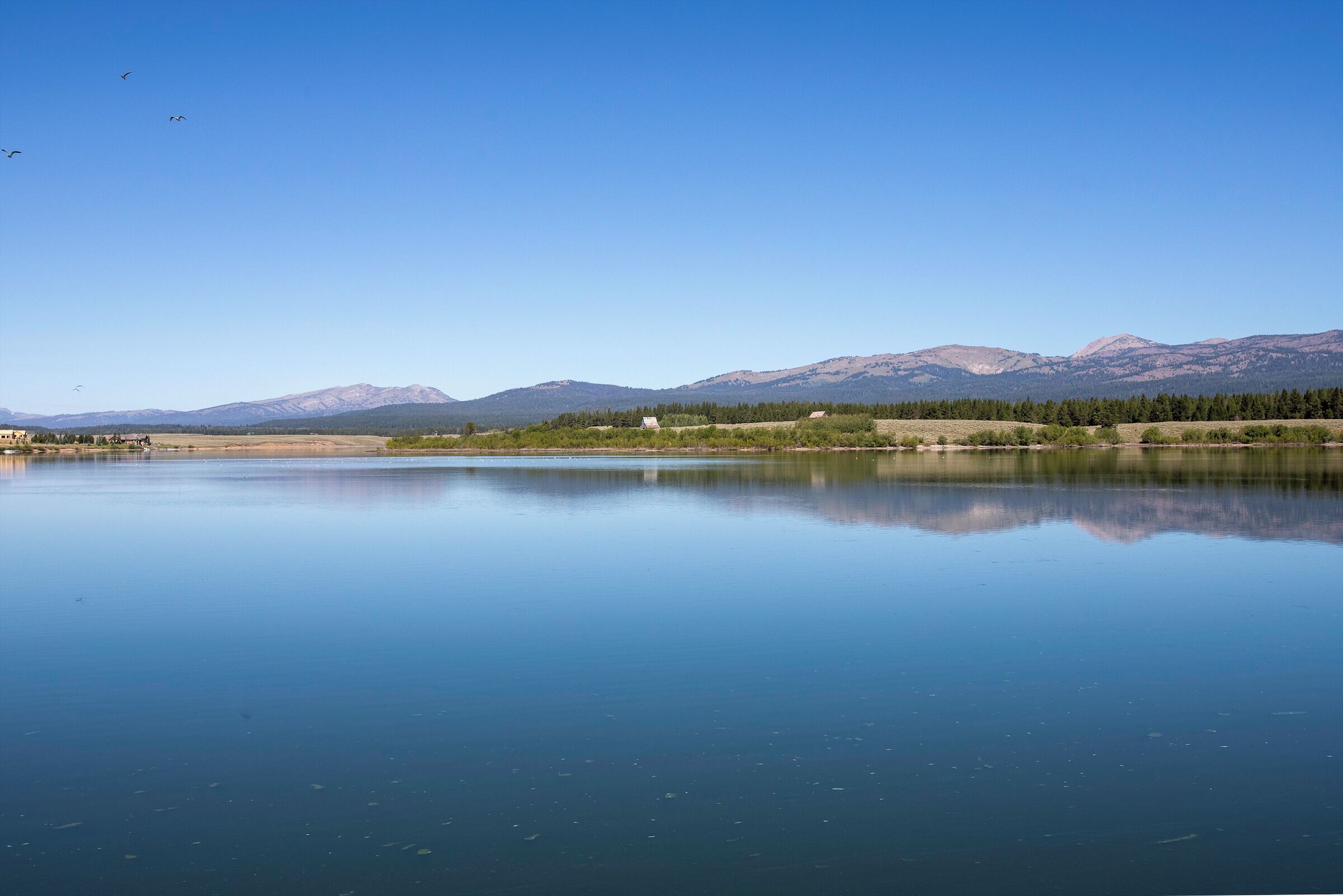 A calm lake with mountains in the background and a clear sky.