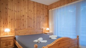 Un dormitorio con paneles de madera, una cama, mesitas de noche y una ventana con cortinas.