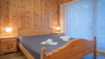 Une chambre aux murs lambrissés, avec un lit, des tables de chevet et une fenêtre avec des rideaux.