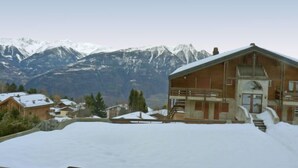 Un edificio de madera con un balcón, rodeado de nieve y montañas al fondo.