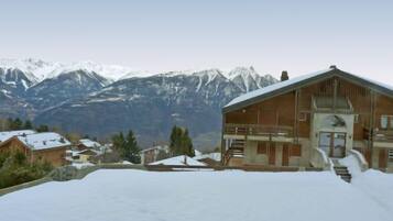 Un bâtiment en bois doté d’un balcon, entouré d’un paysage enneigé et avec des montagnes en arrière-plan.