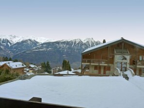A wooden building with a balcony, surrounded by snow-covered ground and mountains in the background.