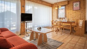 Una habitación acogedora con detalles de madera, un televisor sobre un mueble bajo, una mesa de comedor con sillas y un sofá.