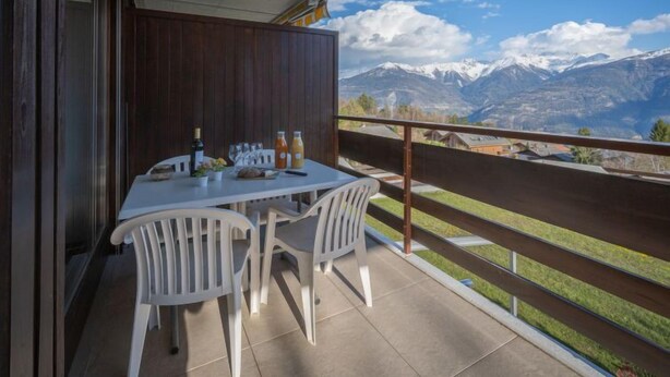 Un balcón con una mesa lista para dos personas, con vistas a un paisaje montañoso.