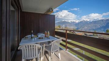 Un balcon avec une table dressée pour deux personnes, offrant une vue sur un paysage montagneux.