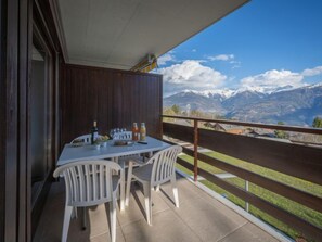 Un balcón con una mesa lista para dos personas, con vistas a un paisaje montañoso.
