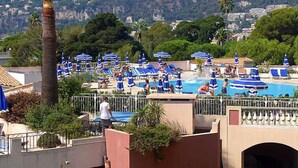 Un espace piscine sur le toit, agrémenté de plusieurs parasols bleus et de chaises longues, entouré de verdure et offrant une vue sur un paysage montagneux.