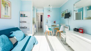 Un salon moderne avec un canapé bleu, un coin repas doté d’une table en verre et un meuble blanc.