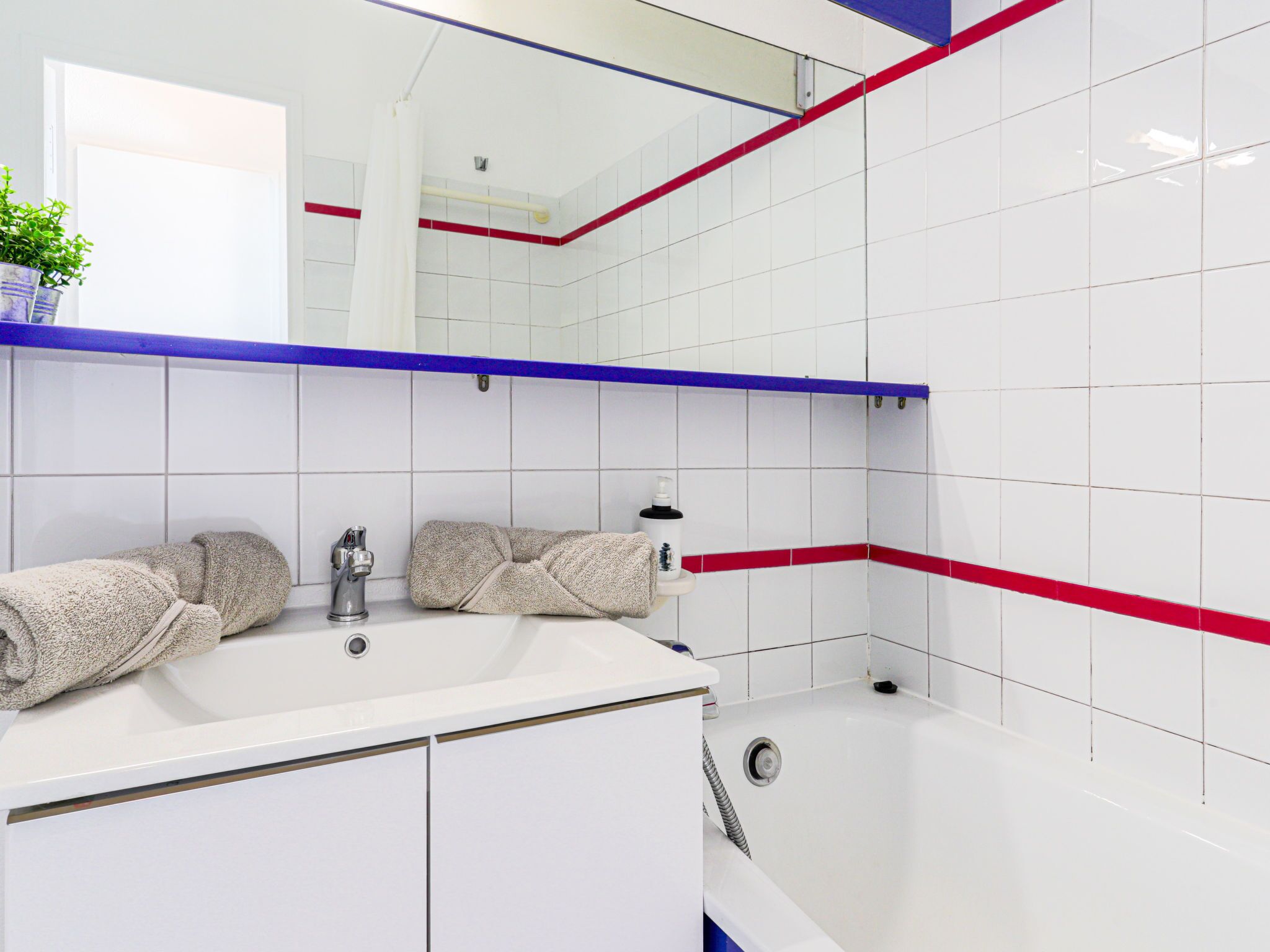 A modern bathroom with white tiles, a bathtub, a sink with a mirror above it, and towels on the counter.