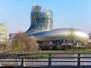 Ein modernes Gebäude mit markanter, geschwungener Architektur und reflektierender Oberfläche, in der Nähe einer Brücke und von Grünflächen umgeben.