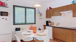 Une cuisine moderne avec des meubles blancs, une table à manger pour quatre personnes et une fenêtre donnant sur un paysage verdoyant.