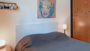 Une chambre à coucher avec un lit, un tableau accroché au mur, une lampe de chevet et une armoire en bois.