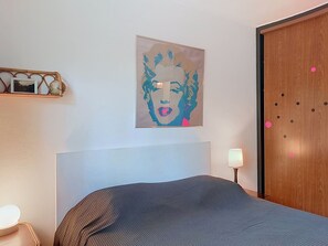 Une chambre à coucher avec un lit, un tableau accroché au mur, une lampe de chevet et une armoire en bois.