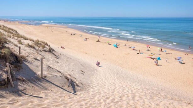 Une vaste plage de sable fin, avec une eau d’un bleu limpide, des parasols et des gens qui profitent du soleil.