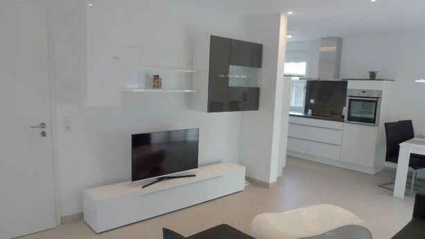 A modern living room with a flat-screen TV, a white sofa, and a dining area with a table and chairs. - Apartment Brake by Interhome (Offenburg)