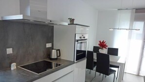 A modern kitchen with a built-in stove, oven, and a dining area with a white table and black chairs. - Apartment Brake by Interhome (Offenburg)