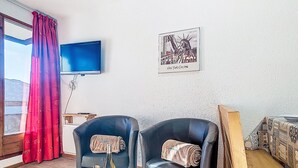 A room with two leather chairs, a wooden table with a bottle and glasses, a TV on the wall, and a framed picture of the Statue of Liberty. - Cimes de Caron 1603 by Interhome (Val Thorens)