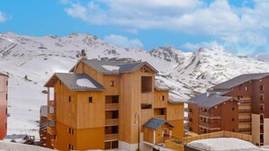 A wooden building with balconies and a snow-covered mountain backdrop. - Cimes de Caron 1603 by Interhome (Val Thorens)