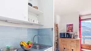 A kitchen with a sink, stove, and microwave. There are cabinets and a window with a view of the mountains. - Cimes de Caron 1603 by Interhome (Val Thorens)