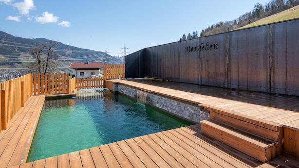 Une terrasse en bois avec une piscine, une clôture en bois et, au fond, un bâtiment portant l’inscription « Morslehen ».