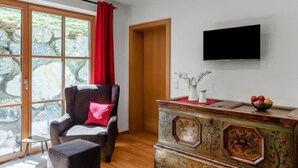 Un salon moderne avec un canapé, un fauteuil rouge, un meuble en bois et un téléviseur fixé au mur.