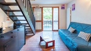 Un salon moderne avec un canapé bleu, un escalier en bois et une vue sur une terrasse extérieure.