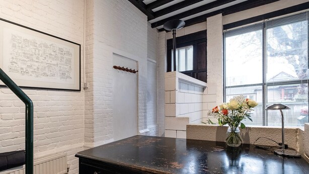 A modern office space with a black desk, white brick walls, and a large window with blinds. - Holly Lodge Coach House by Interhome (London West)