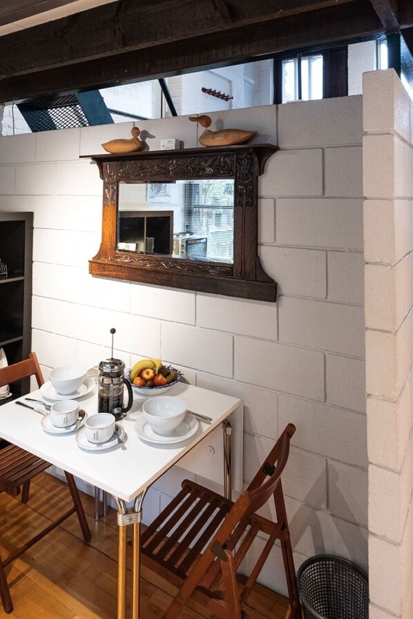 A dining area with a white table, wooden chairs, a coffee pot, and a fruit bowl.