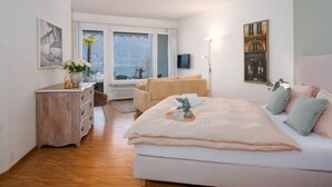 A bedroom with a bed, a dresser, a chair, a TV, and a window with a view. - Double Room Classic by Interhome (Ascona)