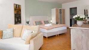 A modern bedroom with a bed, a sofa, a wardrobe, and a dining area with a vase of flowers. - Double Room Classic by Interhome (Ascona)