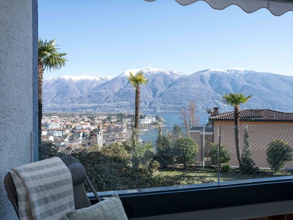 A balcony with a view of a town, mountains, and a lake.