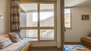 Una habitación acogedora con un ventanal grande, una cama de madera, un banco de madera y una mesita con revistas.