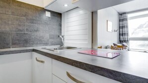 Una cocina moderna con gabinetes blancos, baldosas grises y un lavamanos de acero inoxidable.