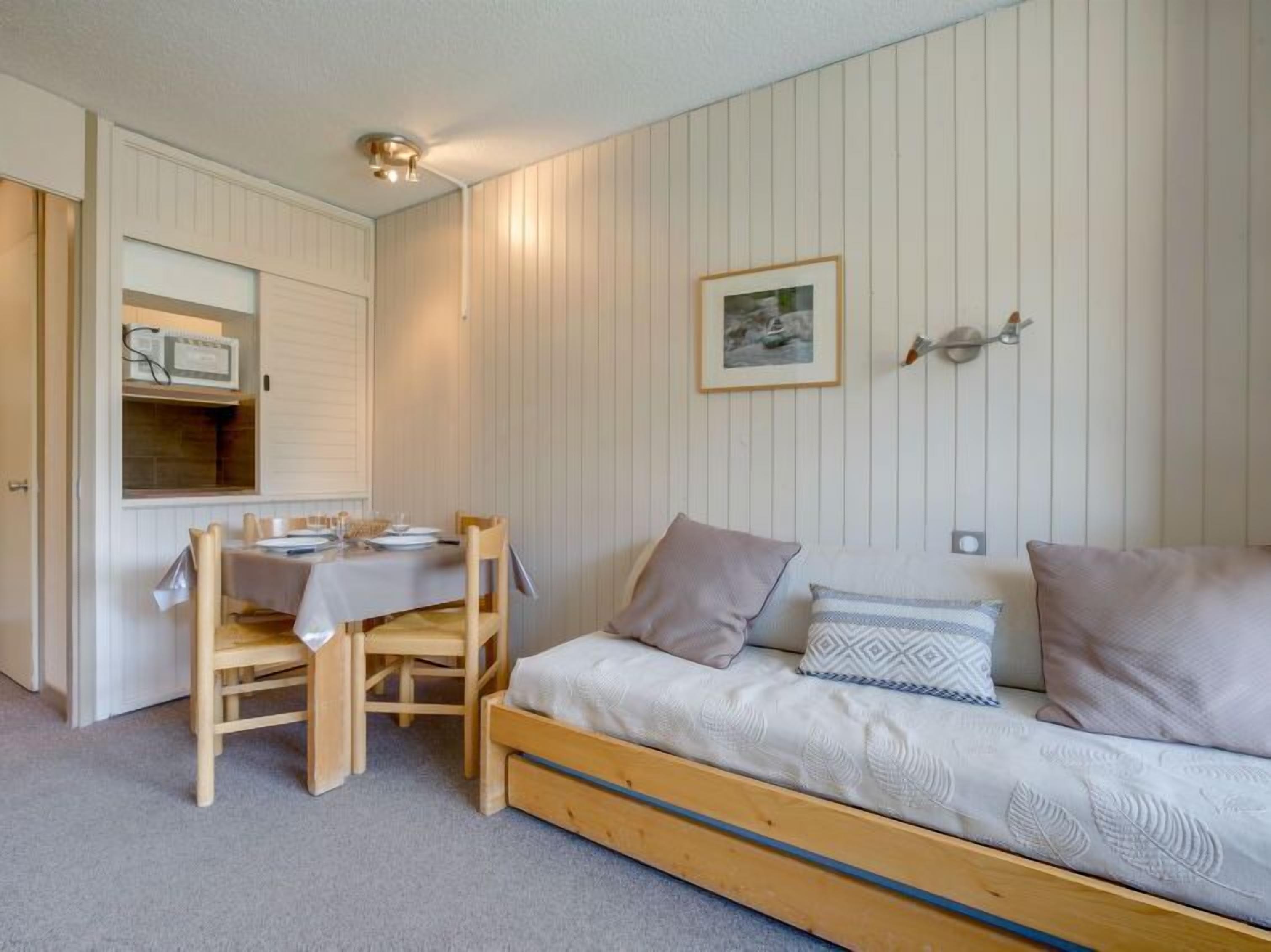 Een compacte kamer met een houten bed, een eettafel met stoelen en een kitchenette.