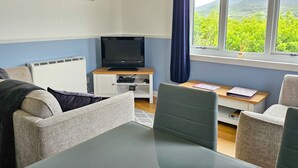 Une chambre avec un lit, un bureau, une télévision et une fenêtre donnant sur un paysage verdoyant.