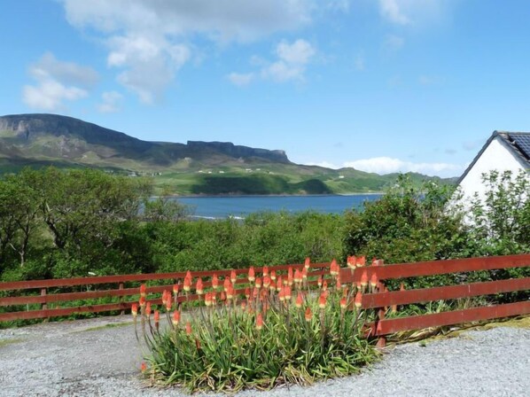 A scenic view of a coastal area with a wooden fence, a body of water, and a hill in the background.