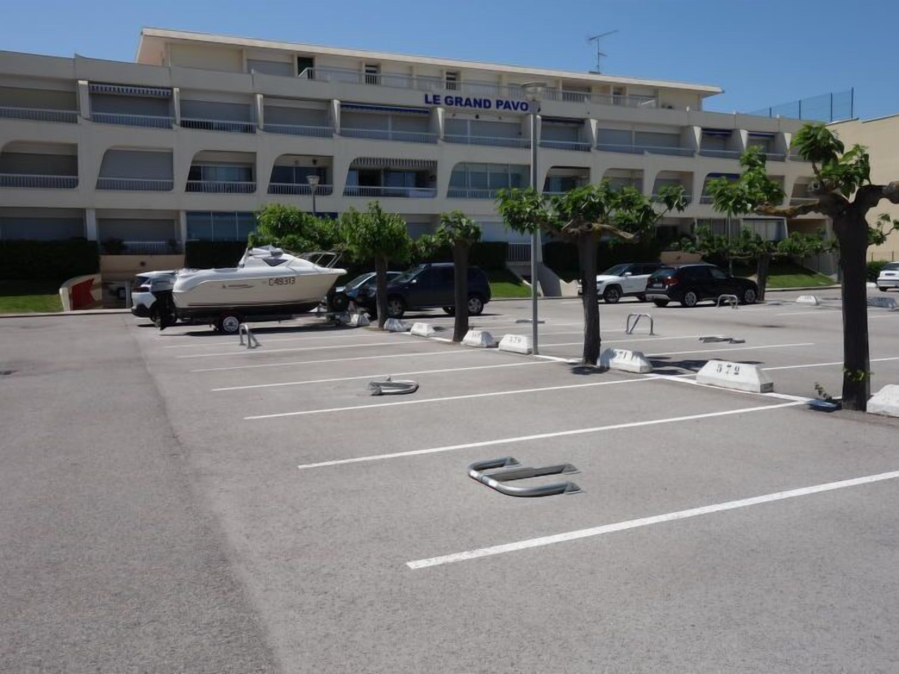 Um estacionamento com vários carros e um barco, em frente a um edifício com a placa 