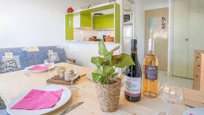 A dining area with a table set for two, a bottle of wine, and a basket of greens. - Le Grand Pavois by Interhome (Port Camargue)