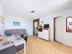 Un coin repas avec une table dressée pour quatre personnes, un canapé, un coin cuisine et une porte donnant sur une autre pièce.