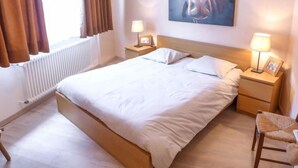 A hotel room with a large bed, two bedside tables with lamps, a chair, and a painting of a cow on the wall. - Barzettes-Vacances 558 / Entrée N° 18 by Interhome (Crans-Montana)