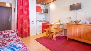 Ein gemütliches Zimmer mit einem Bett, einem Holztisch, einem Fernseher und einer Küchenzeile.