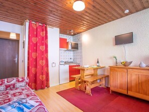A cozy room with a bed, a wooden table, a TV, and a kitchenette. - Sérac B4 by Interhome (Val Thorens)