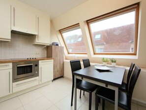 Une cuisine moderne avec un coin repas, dotée d’une grande fenêtre, d’un four encastré et d’une table à manger avec des chaises.
