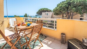 Un balcón con una mesa dispuesta para comer, con vistas a la costa, edificios y árboles.