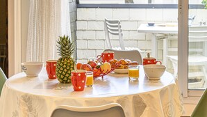 A table set with breakfast items including fruits, croissants, and orange juice, with a view of a white building and a chair in the background. - Les Embruns by Interhome (Carnac)