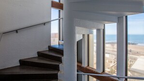 En moderne trappe med gelænder i metal og trætrapper, der fører op til en balkon med udsigt over stranden og havet.