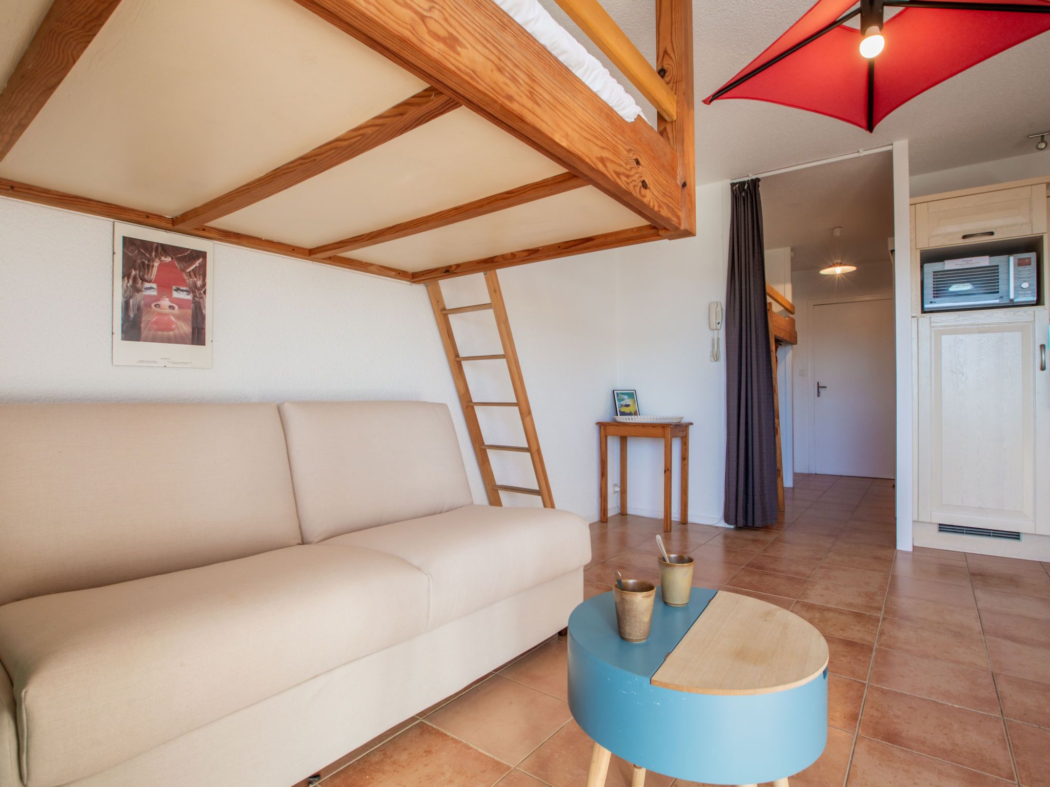 Una habitación acogedora con sofá, una mesita redonda con una taza y un plato, una escalera y un paraguas rojo.