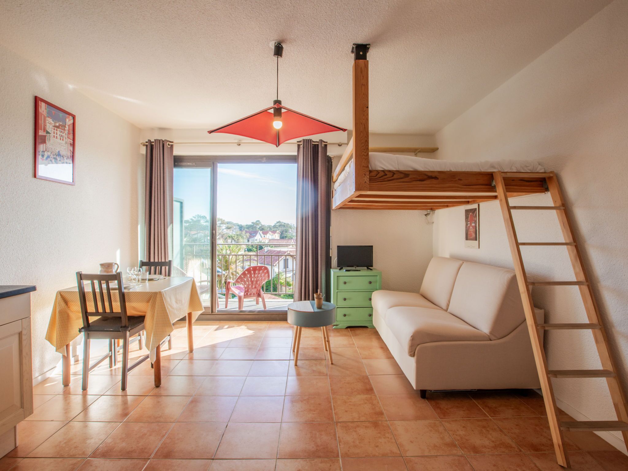 Ein kompakter Wohnraum mit Essbereich, einer Couch, einem Schlafplatz in der Erhöhung und einem Balkon mit Blick.