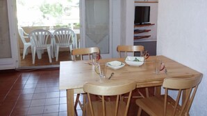 Un coin repas avec une table et des chaises en bois, un saladier en verre et un téléviseur posé sur une étagère.